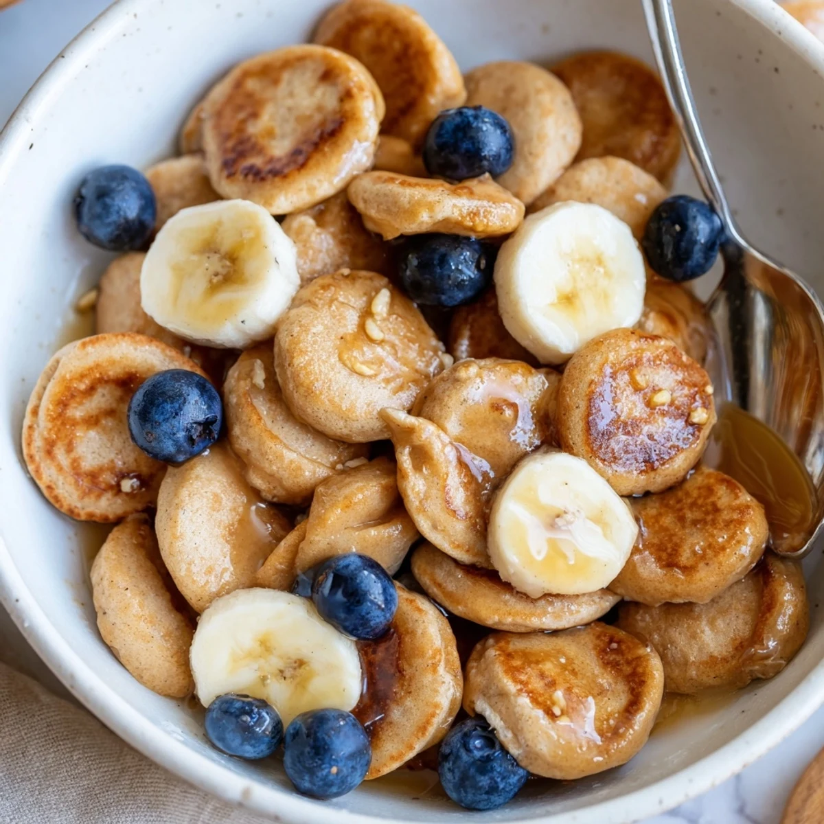 Delicious mini pancake cereal served in a bowl with fresh fruit and syrup.  
