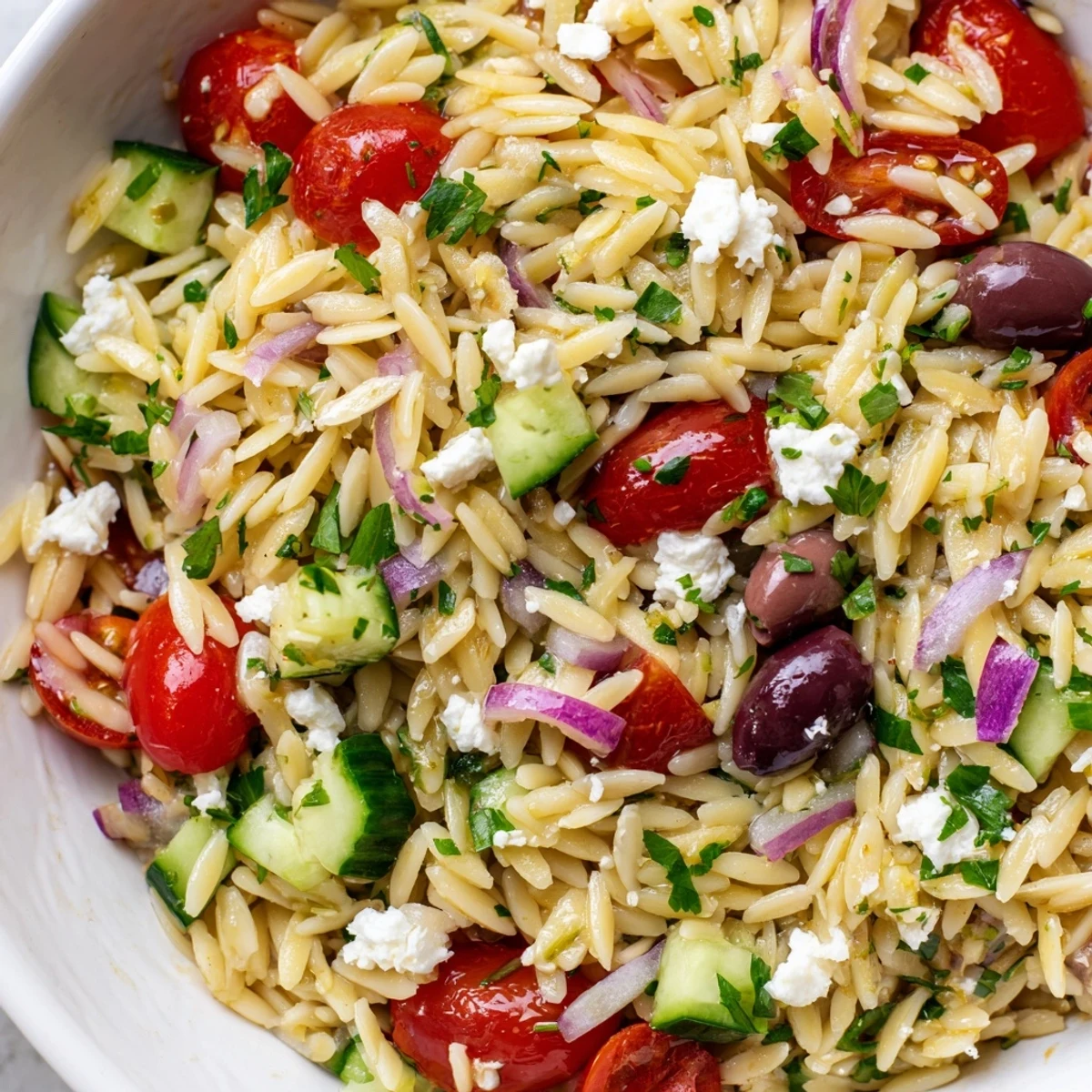 A close-up of Greek Orzo Salad with juicy cherry tomatoes, crisp cucumber, and creamy feta crumbles on a rustic wooden table.