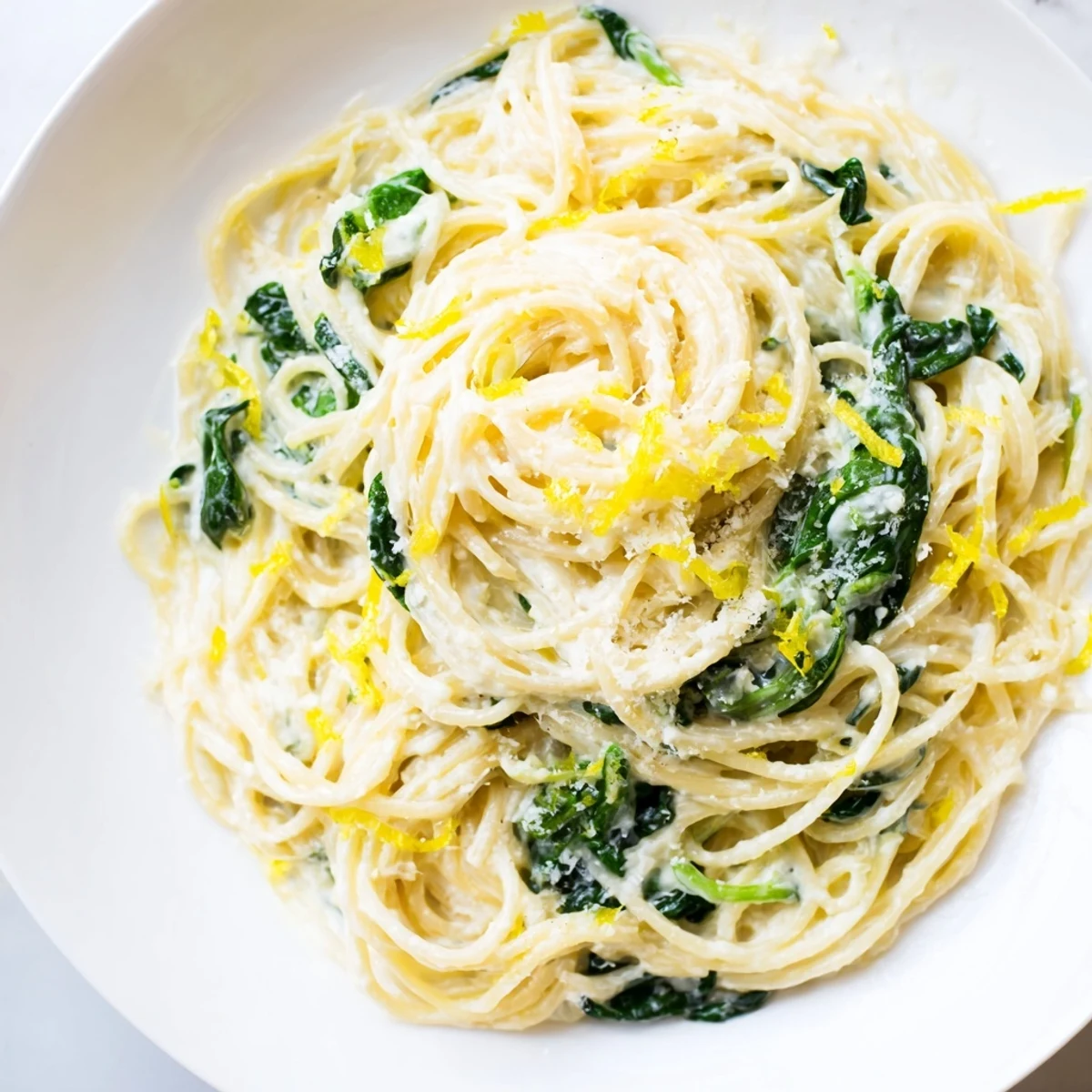 Freshly cooked Creamy Lemon Spinach Spaghetti twirled on a fork, showcasing wilted spinach leaves and a glossy lemon-infused cream sauce.  