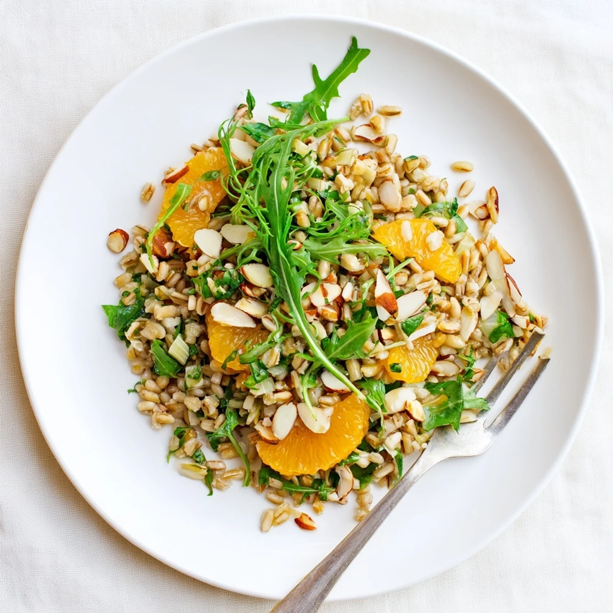 Freshly cooked farro salad with fennel, orange segments, and toasted almonds tossed in citrus vinaigrette on a white plate.