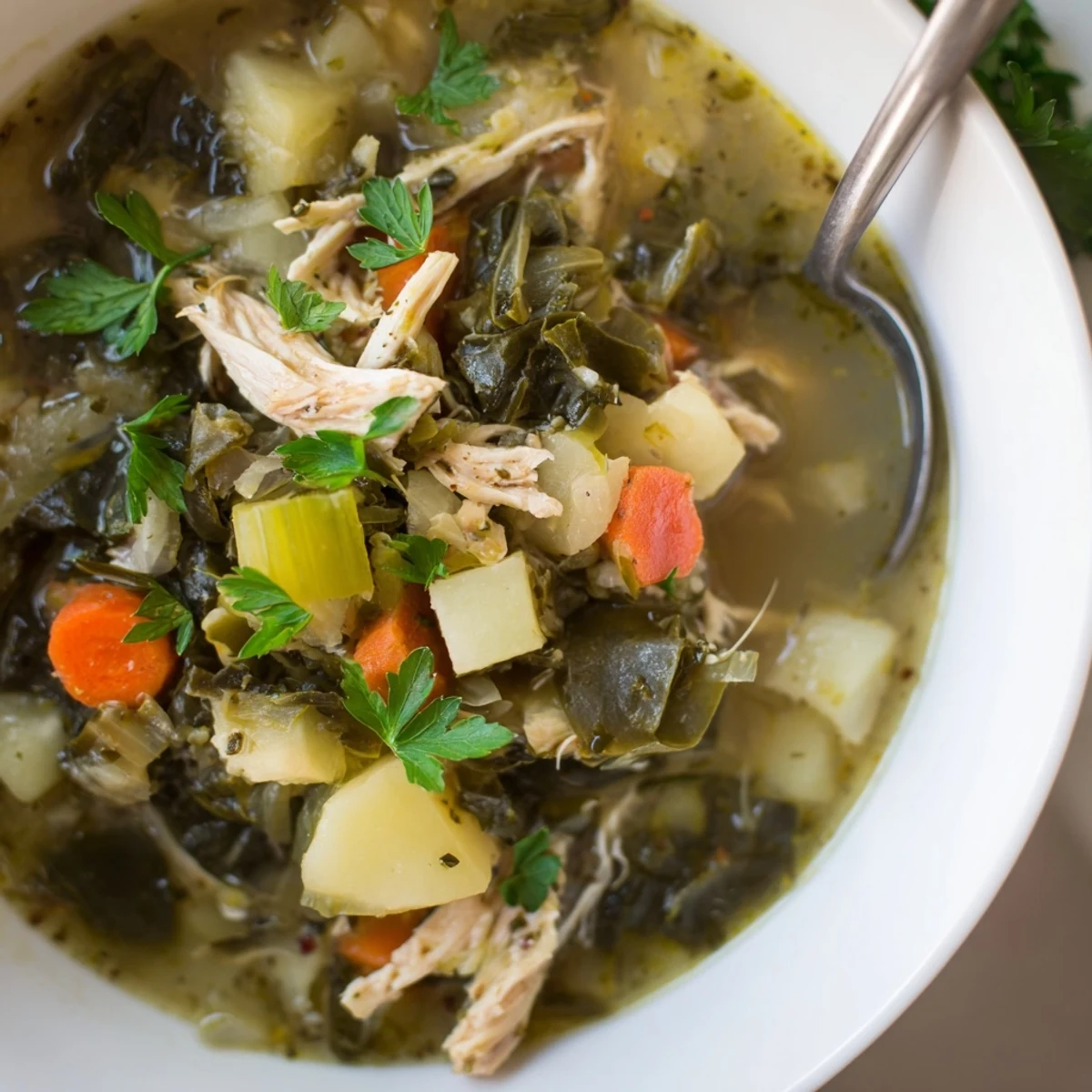 A steaming bowl of Collard Greens, Chicken and Vegetable Soup, featuring tender shredded chicken, diced potatoes, and bright greens in a savory broth.