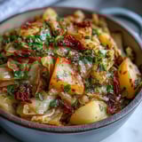 Tender braised cabbage with potatoes and chili, buttery and soft, served steaming from a rustic pot for a cozy meal.