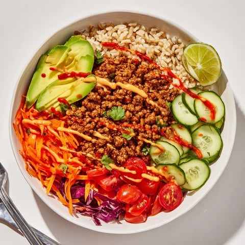 A colorful plant-based meat bowl topped with fresh veggies and creamy sauce.  
