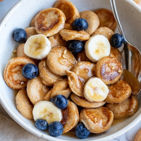 Delicious mini pancake cereal served in a bowl with fresh fruit and syrup.  