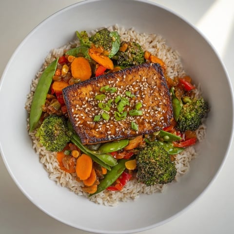 Golden-brown pressed tofu steaks sit atop vibrant stir-fried vegetables, ready to enjoy with fluffy rice.