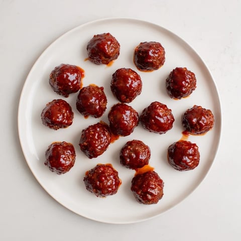 Baked cherry-glazed meatballs glistening with a sweet, tangy sauce, perfect for party appetizers.