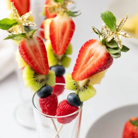 Festive champagne flute fruit garnishes featuring fresh strawberries, kiwi, pineapple, and berries displayed.