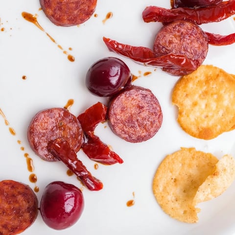 Sizzling chorizo and sweet cherries artfully arranged in The Crimson Tide appetizer on crisp crackers.