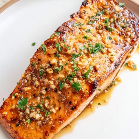 Glossy honey garlic glazed salmon fillets roasted to perfection, garnished with fresh parsley and served with lemon wedges.