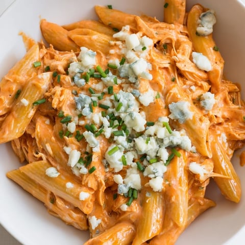 Golden penne pasta swirls in a creamy, spicy Buffalo Chicken Pasta, topped with crumbled blue cheese and fresh chives.