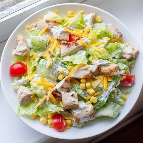 A close-up of Ranch Chicken Chopped Salad in a white bowl, featuring crisp romaine, diced chicken, sweet corn, and cherry tomatoes drizzled with creamy ranch dressing.