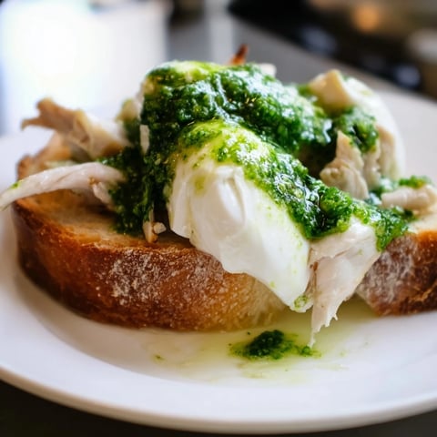 Golden toasted sourdough slices are generously slathered with vibrant green pesto and topped with tender, thinly sliced chicken, then crowned with creamy, torn burrata cheese.