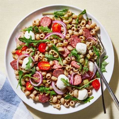 Fresh Spring Antipasto Pasta Salad in a white bowl, ditalini pasta mixed with bright arugula, cherry tomatoes, and mozzarella pearls.