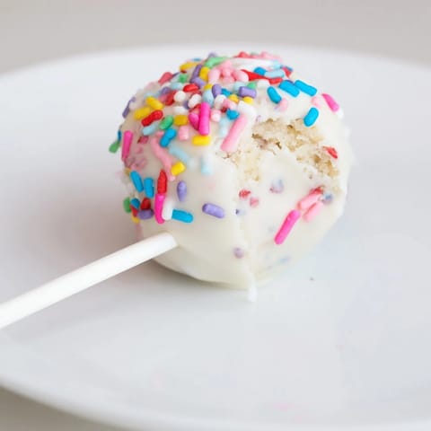 A close-up of a dreamy Lightened-Up Sugar Cookie Cake Pop, showing its creamy chocolate coating and colorful sprinkles.