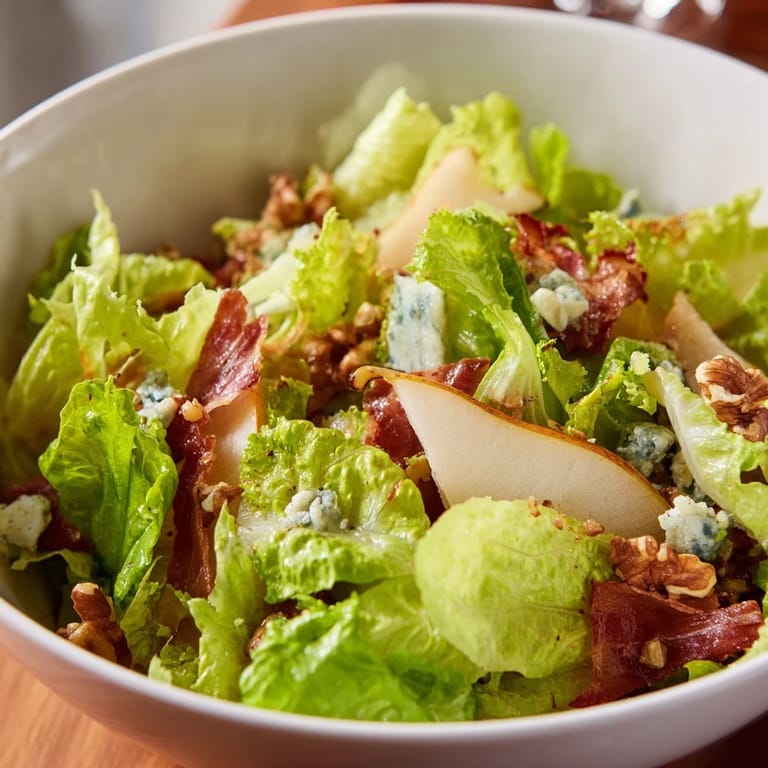This fresh salad combines crisp frisée, ripe pear slices, and crumbled blue cheese, finished with crunchy walnuts and savory prosciutto.