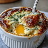 "Easter Eggs en Cocotte with creamy herbed custard and parmesan, baked in individual ramekins for a festive brunch."